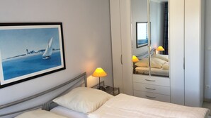 Una habitación de hotel con cama, armario, un cuadro y una lámpara.