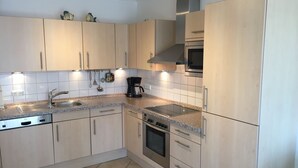 Una cocina moderna con gabinetes de colores claros, un lavamanos de acero inoxidable, un horno empotrado y un microondas.