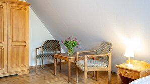 A room with a wooden wardrobe, two patterned chairs, a small table with a vase of flowers, and a bedside table with a lamp. - (STR47a) Holiday apartment "Heitmann" - Holiday apartment "Heitmann" up to 4 persons (Timmendorfer Strand)