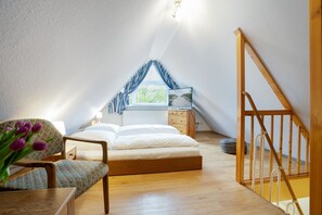 Un dormitorio acogedor en el ático con cama, una silla, un escritorio y una ventana con cortinas.