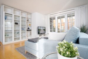 Een moderne woonkamer met een grijze bank, een flatscreen televisie en een wit kastje met glazen deuren.