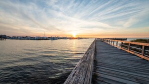 Eine Holzstege, der sich in ruhiges Wasser erstreckt, mit einem Sonnenuntergang im Hintergrund.