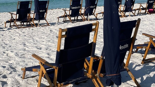 Strandstühle und Sonnenschirme an einem sandigen Strand mit dem Meer im Hintergrund.