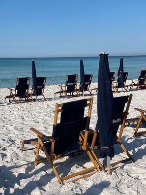 Des chaises de plage et des parasols sur une plage de sable, avec l’océan en arrière-plan.