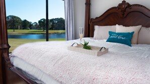 Ein Schlafzimmer mit großem Fenster und Blick auf einen See und Bäume.
