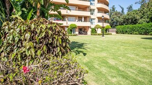 A multi-story building with balconies, a well-maintained lawn, and surrounding greenery.