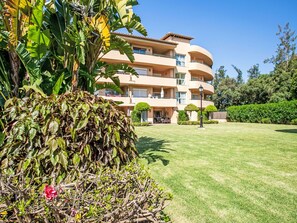A multi-story building with balconies, a well-maintained lawn, and surrounding greenery.