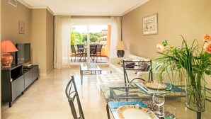 A living room with a sofa, TV, glass coffee table, and a dining area with chairs and a table.