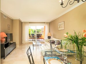 A living room with a sofa, TV, glass coffee table, and a dining area with chairs and a table.