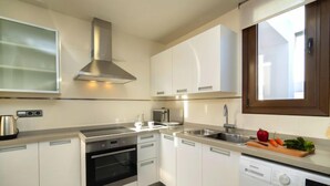 Una cocina moderna con armarios blancos, electrodomésticos de acero inoxidable, horno empotrado, microondas y lavadora.