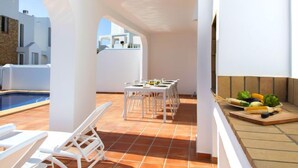Una terraza en la azotea con piscina, mobiliario blanco y una mesa lista para comer.