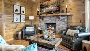 A cozy log cabin interior with a stone fireplace, leather furniture, and framed wildlife pictures. - Majestic 3BR Smoky Cabin + Views + Small Pet Friendly + Games + Near Dollywood (Pigeon Forge)