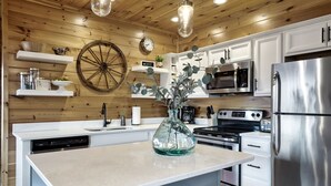 A kitchen with wooden walls, white cabinetry, a central island, a large clock, and modern appliances. - Majestic 3BR Smoky Cabin + Views + Small Pet Friendly + Games + Near Dollywood (Pigeon Forge)