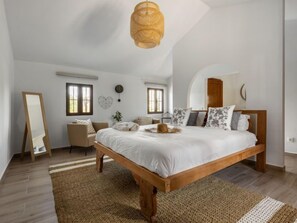 Um quarto espaçoso com uma grande cama de madeira, um lustre pendente e um espelho na parede.