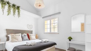 Un dormitorio moderno con una cama, mesitas de noche, una planta colgante, una ventana y un espejo.