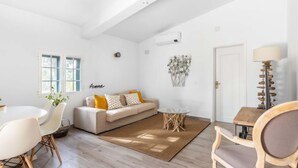 Un interior luminoso y blanco con un sofá, una mesa de comedor redonda y una silla de madera.