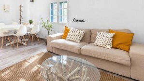 Una sala de estar moderna con un sofá color beige, una mesa de centro de vidrio y un comedor con una mesa y sillas blancas.