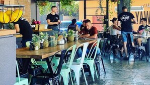 A restaurant with a brick wall, hanging plants, and a mix of wooden and plastic chairs. - The Parap Markets Stay | Walk to Markets & Cafés (Parap)