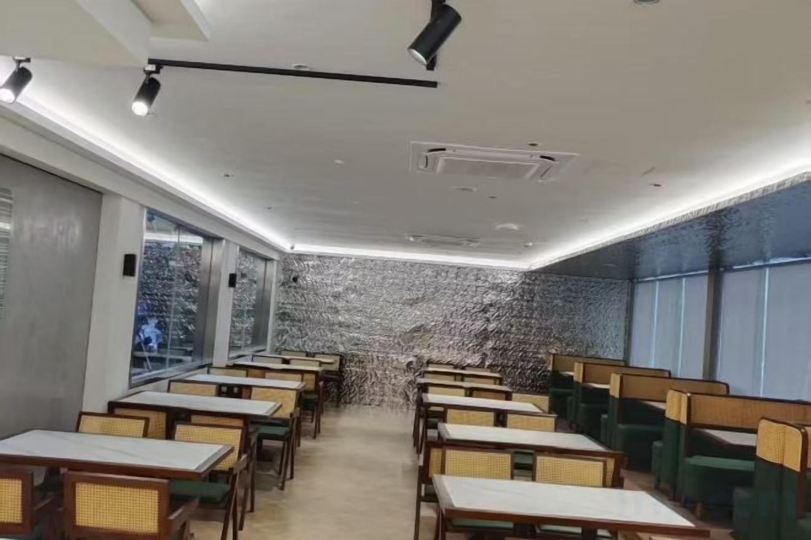 Un restaurante con varias mesas y cabinas, una pared con diseño y ventanas amplias.