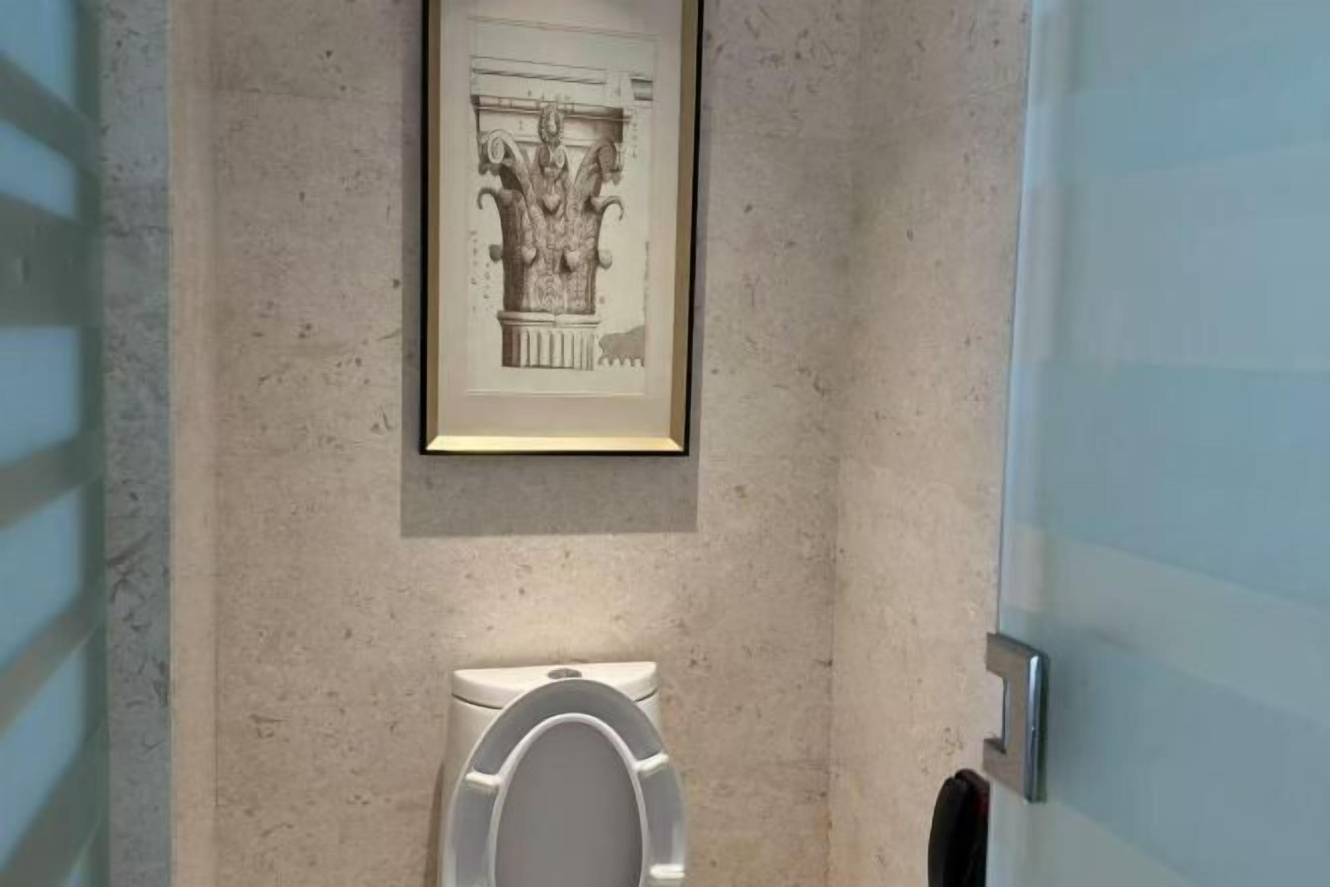 Um banheiro moderno com vaso sanitário, um desenho arquitetônico emoldurado na parede e uma porta de vidro.