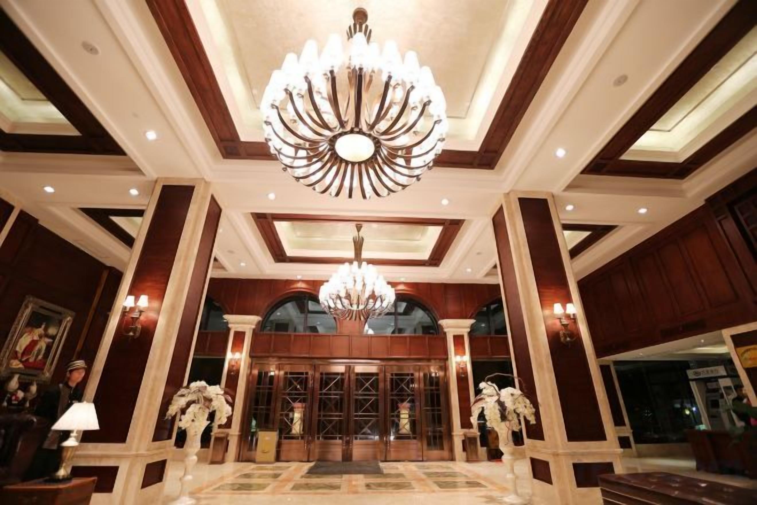 A grand lobby with a large chandelier, marble flooring, and a reception desk.