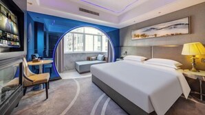 Moderni hotellihuone, jossa on suuri sänky, työpöytä, oleskelualue ja televisio.