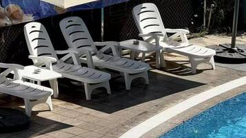A poolside area with white plastic lounge chairs and a small table, surrounded by a tiled deck.