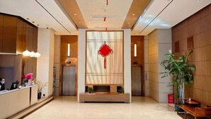 Un vestíbulo de hotel moderno con una recepción, un elemento decorativo rojo grande en la pared y una zona de estar con un banco.