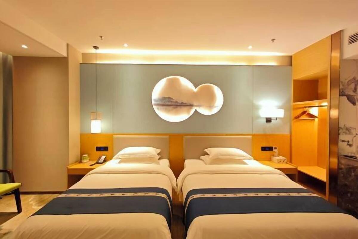 Habitación de hotel con dos camas, una lámpara fijada a la pared y una mesita con una silla.