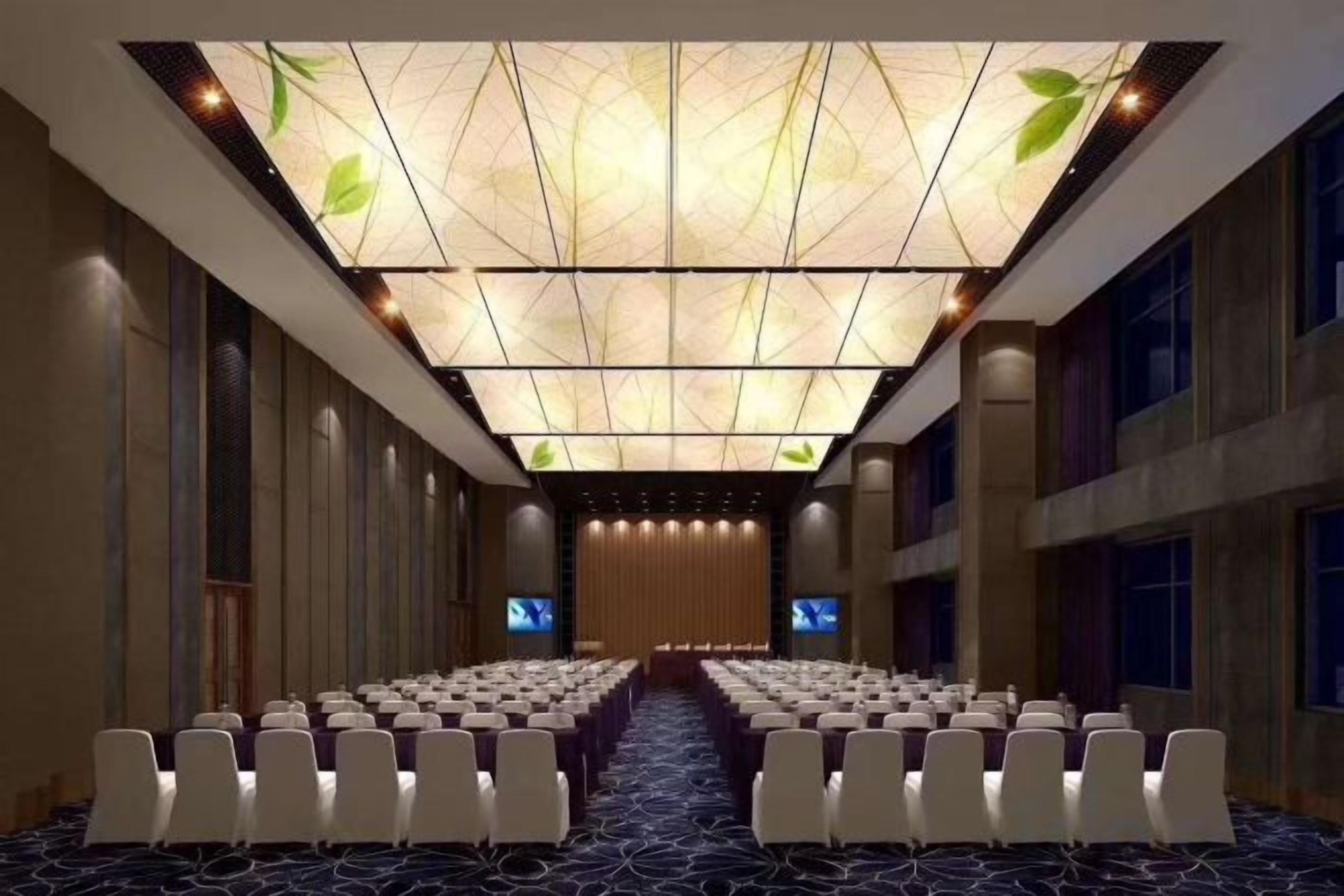 Un salón de conferencias con filas de sillas blancas, una alfombra estampada y un techo con diseños de hojas.