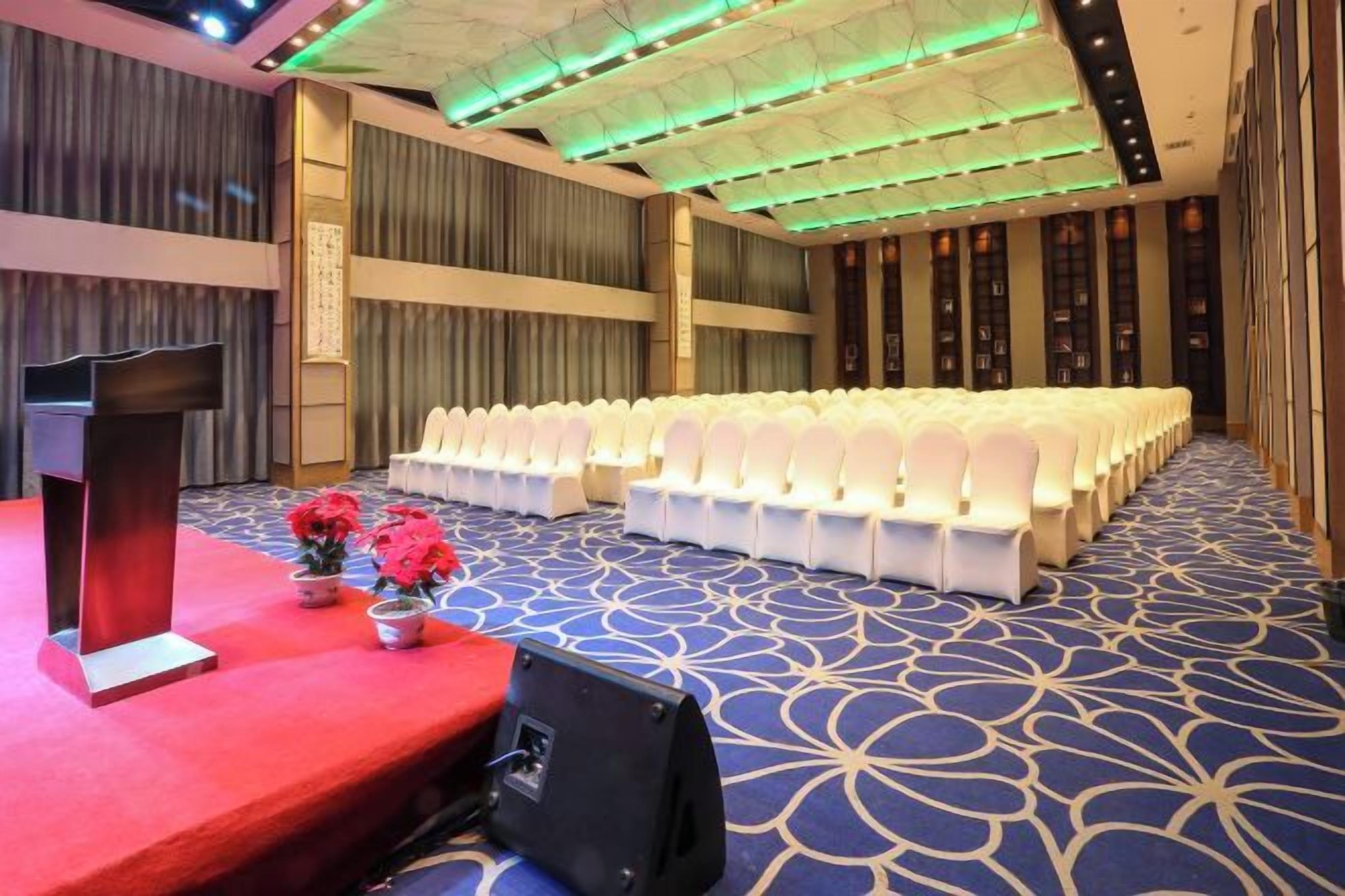 A conference room with rows of white chairs, a podium, and a carpeted floor.