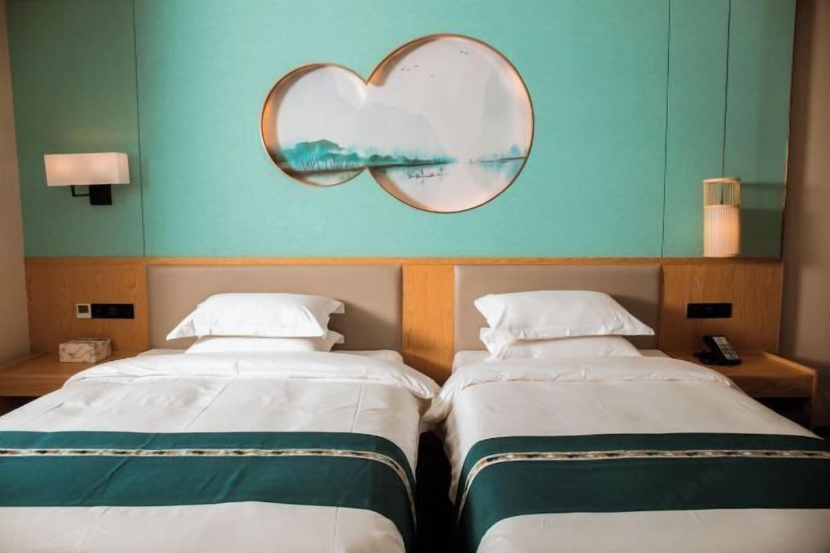 A hotel room with two beds, a heart-shaped artwork on the wall, a nightstand with a lamp, and a small table with a phone.