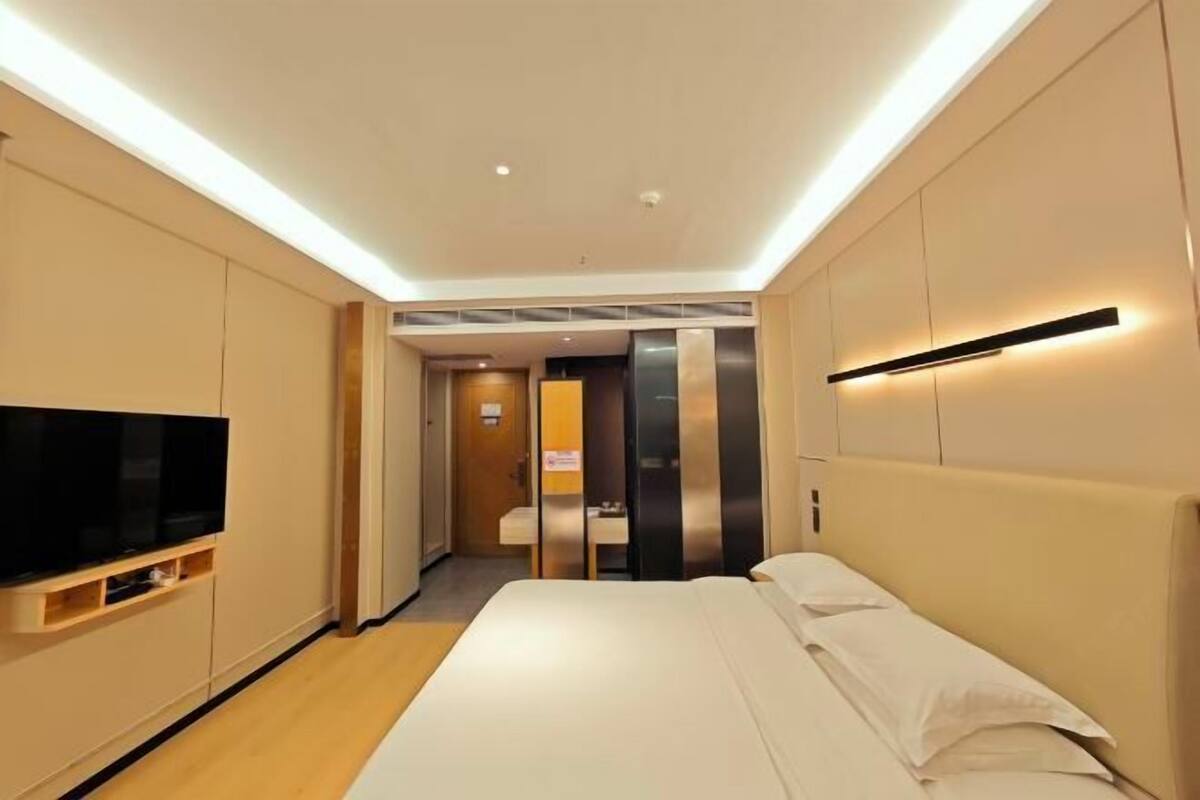Habitación de hotel con cama, televisor montado en la pared y pasillo que conduce a otra habitación.