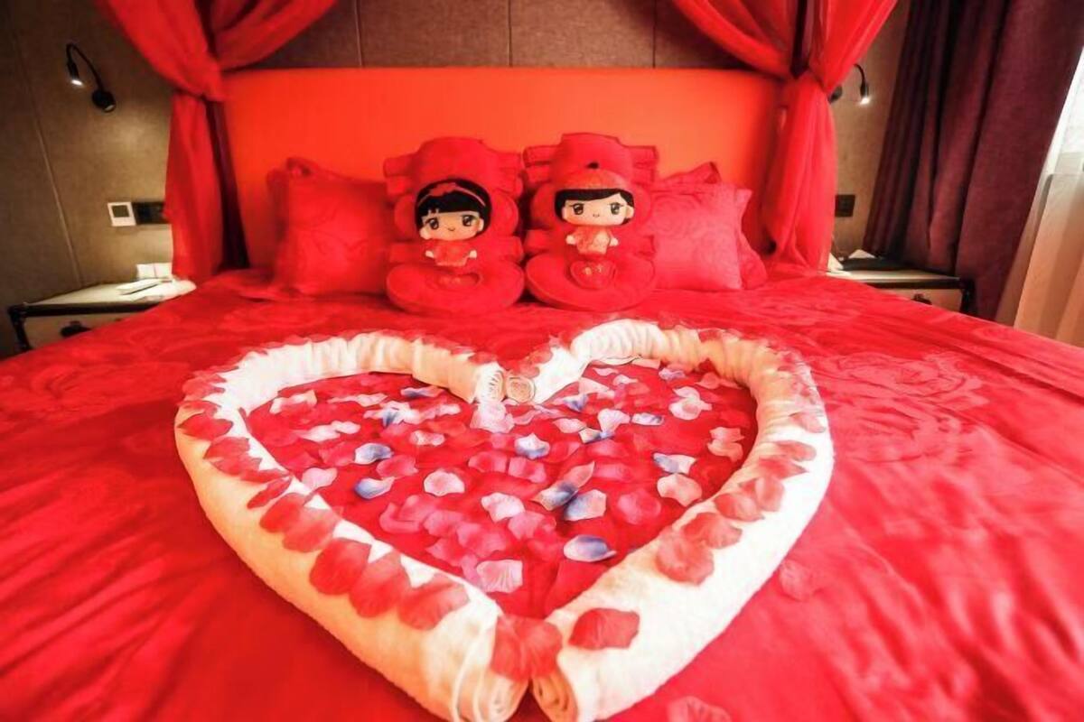 Una cama con una colcha con forma de corazón y dos almohadones rojos con figuritas.
