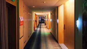 Un pasillo de hotel con puertas a ambos lados, algunas con letreros, y un cartel de salida verde sobre una puerta a la izquierda.