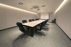 Un salón de conferencias con una larga mesa y sillas, piso alfombrado e iluminación empotrada.
