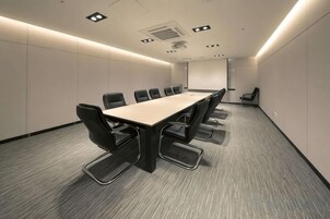Un salón de conferencias con una larga mesa y sillas, piso alfombrado e iluminación empotrada.