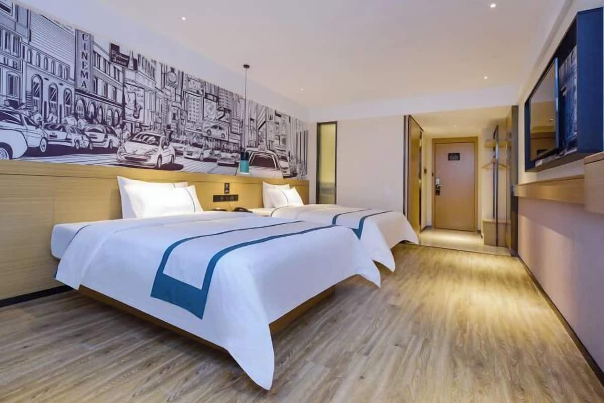 A hotel room with a large bed, a wall mural, and a hallway leading to another room.