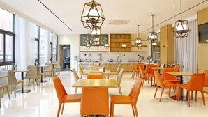 Un comedor moderno con mesas y sillas, una cocina al fondo y ventanas amplias.