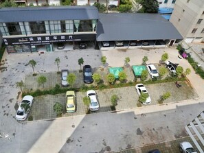 An aerial view of a parking lot with several cars, a building with a sign, and a fenced area with trees. - City Convenient Hotel (Yuxi)