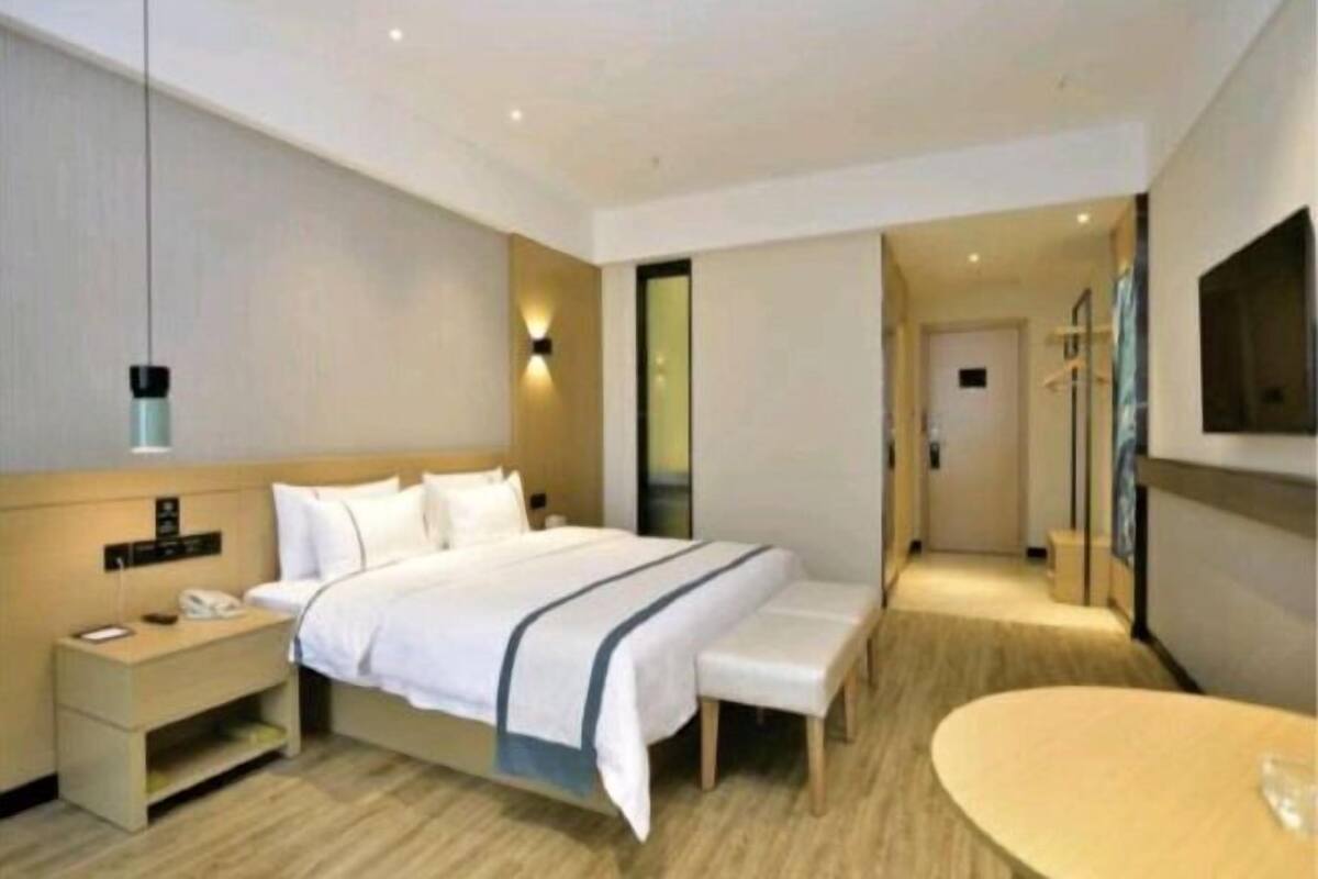 A modern hotel room with a large bed, bedside table, bench, and a TV mounted on the wall.