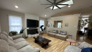 Ein geräumiges Wohnzimmer mit einem großen Flachbildfernseher, Deckenventilator und Kamin. Zwei Sofas und ein Couchtisch sind ebenfalls vorhanden.