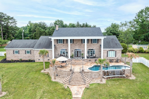 Una casa grande con piscina, un patio y una escalera de piedra que lleva a la entrada.