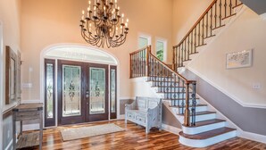 Ein geräumiges Foyer mit Holzboden, einer imposanten Treppe und einem Chandelier.