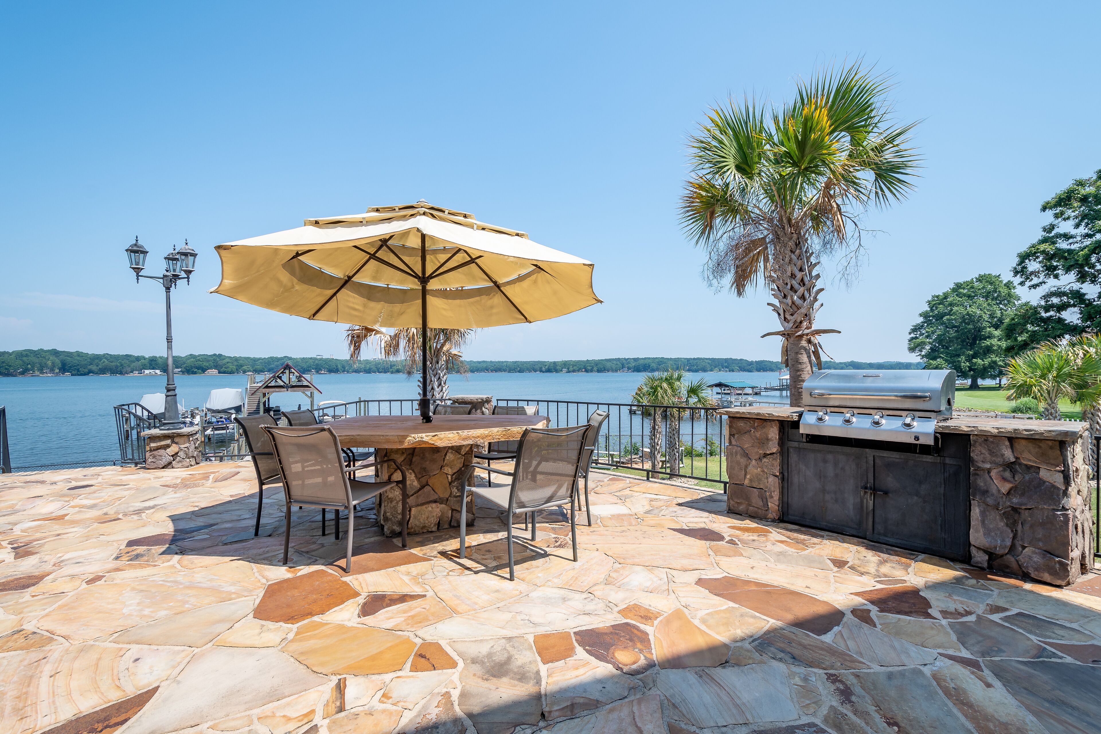 An outdoor patio with a stone table and chairs, a grill, and a view of the lake.