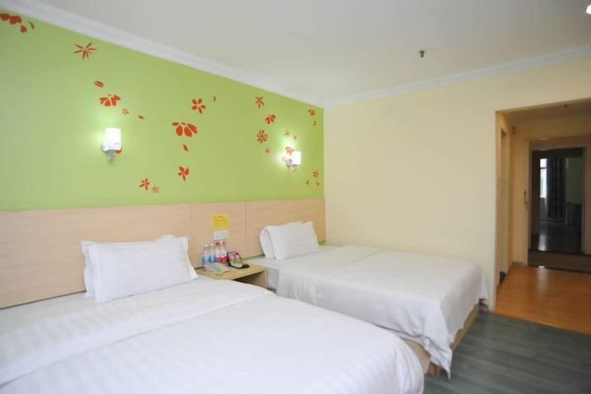 A hotel room with two beds, a green wall with floral decals, and a wooden headboard.