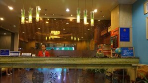 A hotel reception area with a receptionist, a digital display, and a reception desk. - Yuekai Hostel (Dongguan)