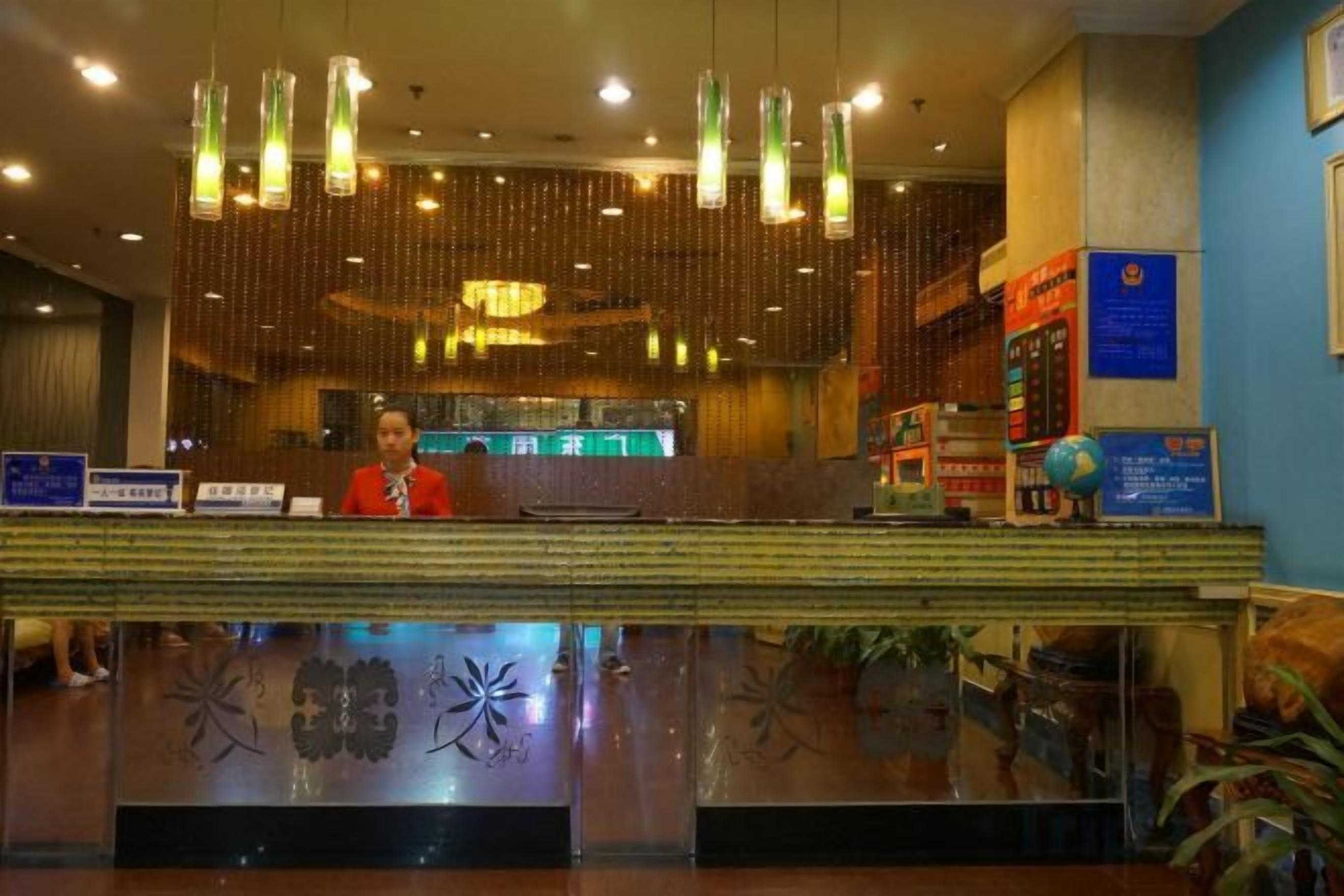 A hotel reception area with a receptionist, a reception desk, and a decorative wall with a globe and informational signs.