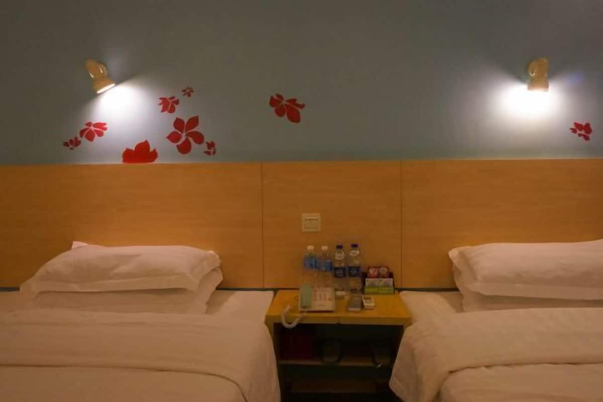 A hotel room with two beds, a wooden headboard, wall-mounted lights, and a small table with toiletries.