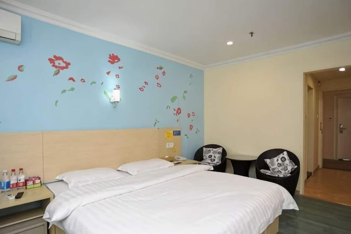 A hotel room with a bed, a desk with a chair, a wall-mounted phone, and a door.